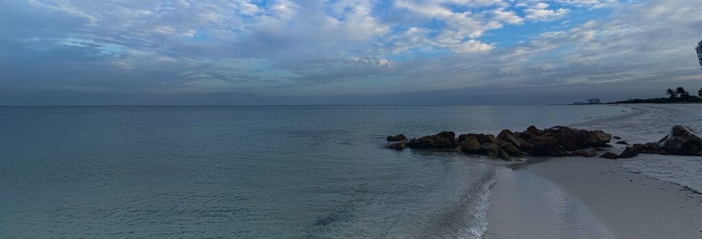 A Gulf beach in Naples, Florida, with a rock jetty and Gulf front buildings on the horizon